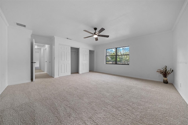 unfurnished bedroom featuring two closets, ornamental molding, light colored carpet, and ceiling fan