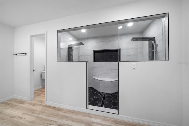 bathroom with tiled shower, toilet, and hardwood / wood-style floors