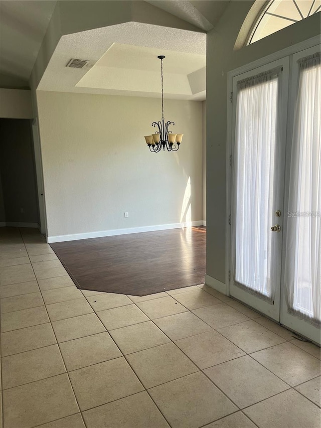 tiled spare room featuring a notable chandelier, a raised ceiling, and french doors