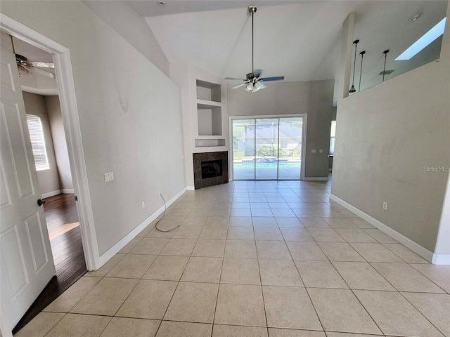 unfurnished living room with a tile fireplace, built in features, light tile patterned floors, ceiling fan, and a healthy amount of sunlight