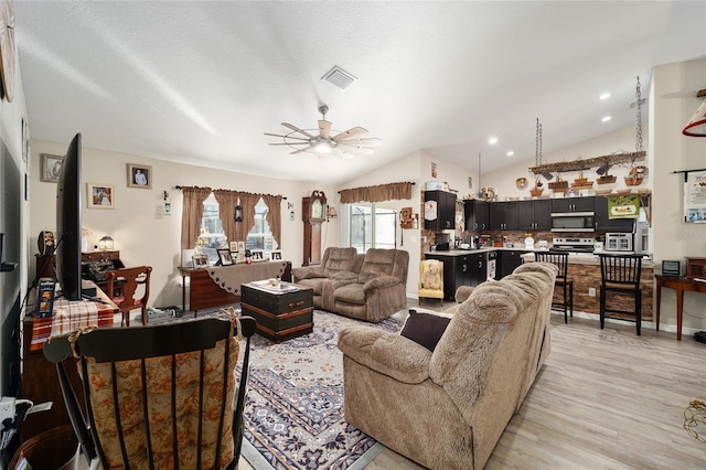 living room with ceiling fan, vaulted ceiling, a textured ceiling, and light wood-type flooring