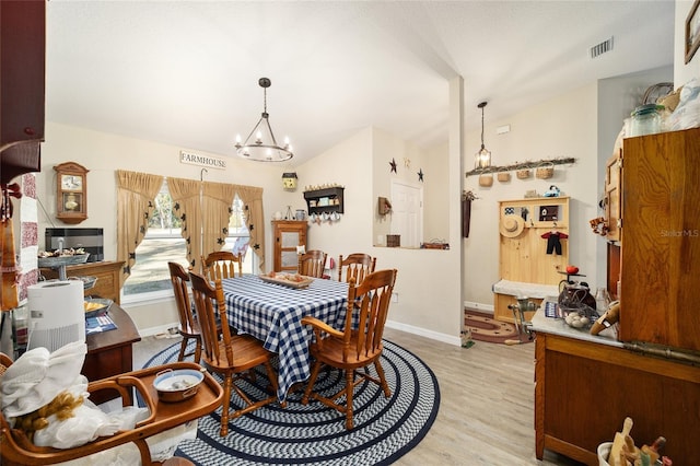 dining space with an inviting chandelier, lofted ceiling, and light wood-type flooring