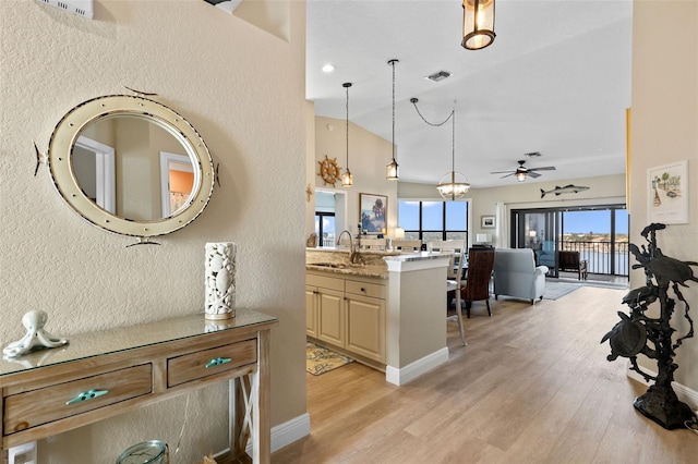 interior space with sink, light stone counters, vaulted ceiling, pendant lighting, and light hardwood / wood-style floors