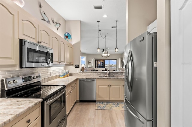 kitchen featuring appliances with stainless steel finishes, pendant lighting, sink, decorative backsplash, and light wood-type flooring