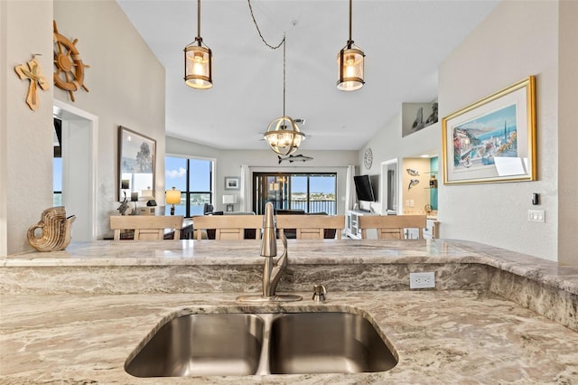 kitchen featuring light stone counters, sink, decorative light fixtures, and vaulted ceiling