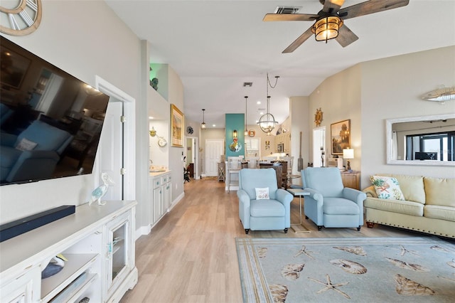 living room with ceiling fan with notable chandelier, vaulted ceiling, and light hardwood / wood-style flooring