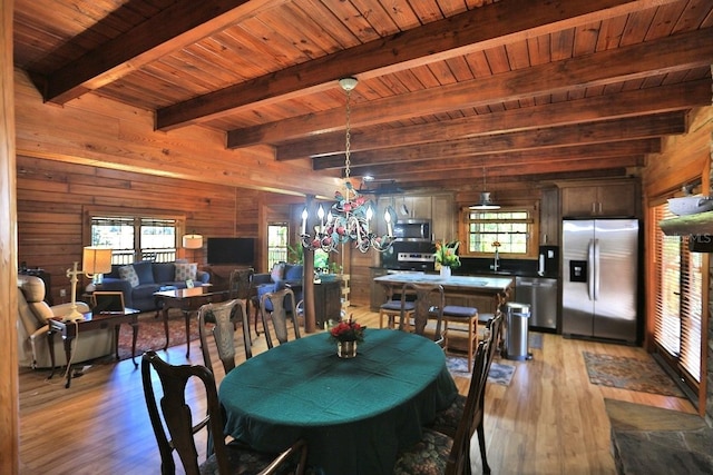 dining room with sink, a notable chandelier, wooden walls, and light hardwood / wood-style floors