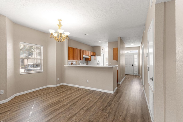 kitchen with an inviting chandelier, white refrigerator with ice dispenser, kitchen peninsula, and wood-type flooring