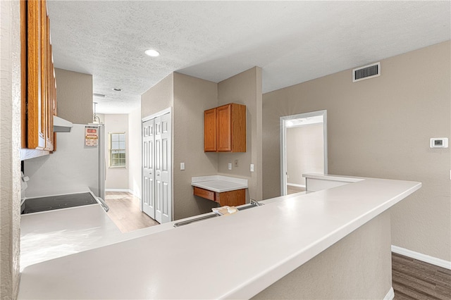 kitchen with hardwood / wood-style flooring, exhaust hood, range, kitchen peninsula, and a textured ceiling