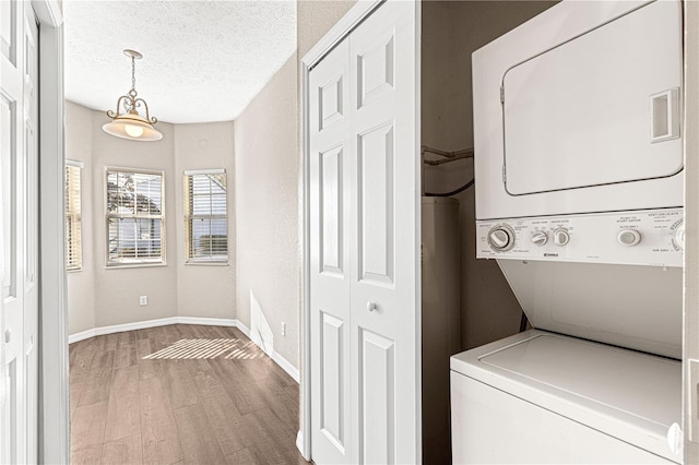 clothes washing area featuring stacked washer / drying machine, a textured ceiling, and light wood-type flooring