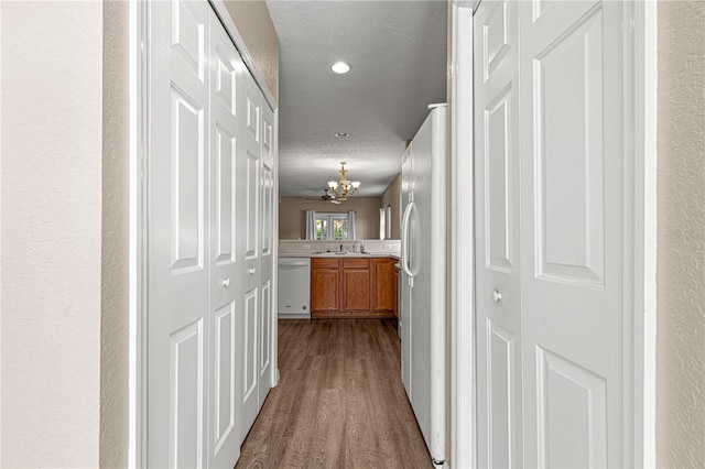 hall featuring wood-type flooring, sink, a textured ceiling, and a notable chandelier