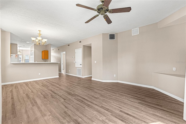 unfurnished living room featuring wood-type flooring, ceiling fan with notable chandelier, and a textured ceiling