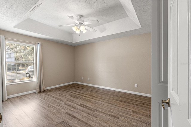 empty room featuring ceiling fan, wood-type flooring, a raised ceiling, and a textured ceiling