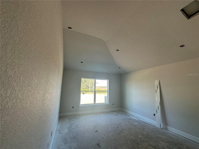 spare room featuring a textured wall, a textured ceiling, and baseboards