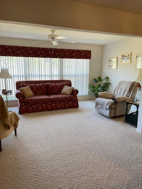 living area featuring beamed ceiling, ceiling fan, and carpet floors