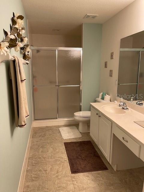 bathroom featuring a shower with door, vanity, a textured ceiling, and toilet