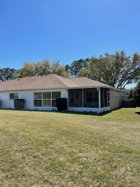 rear view of property with stucco siding, a lawn, and a sunroom