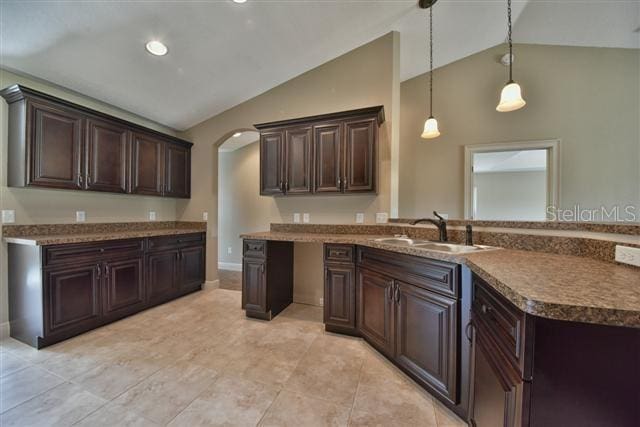 kitchen with pendant lighting, lofted ceiling, dark brown cabinetry, and sink