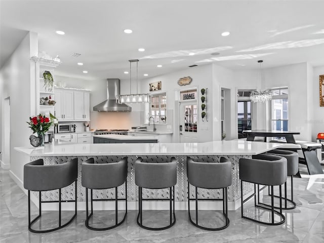 kitchen with sink, a breakfast bar area, white cabinetry, decorative light fixtures, and wall chimney range hood