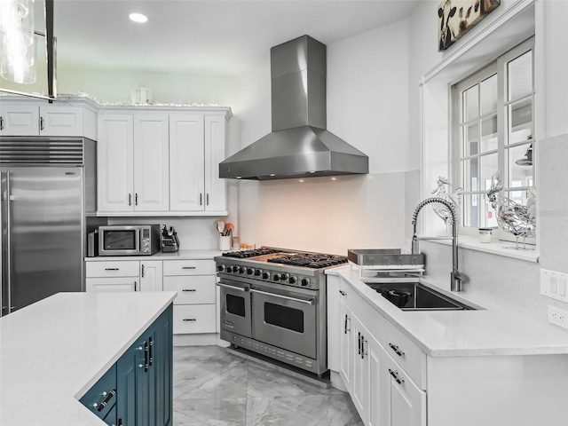 kitchen featuring wall chimney exhaust hood, blue cabinets, sink, high end appliances, and white cabinets