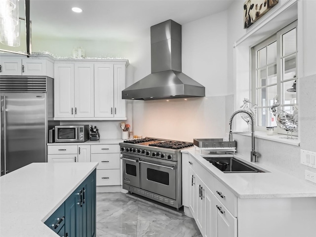 kitchen with white cabinets, marble finish floor, high end appliances, a sink, and wall chimney range hood