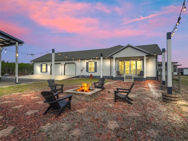 rear view of property featuring driveway, a garage, a fire pit, and covered porch