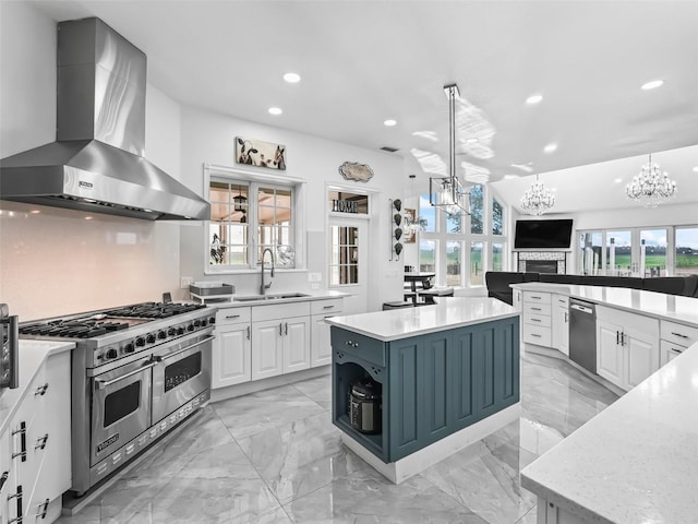 kitchen with a sink, a chandelier, white cabinetry, stainless steel appliances, and wall chimney range hood