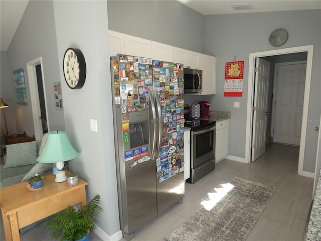 kitchen featuring white cabinetry, stainless steel appliances, light stone countertops, and vaulted ceiling