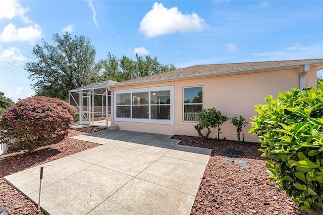 back of house featuring a patio, stucco siding, and glass enclosure