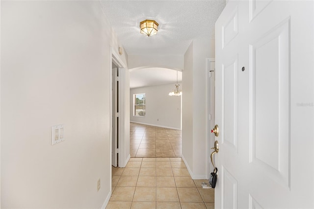 hall with light tile patterned floors, baseboards, arched walkways, an inviting chandelier, and a textured ceiling