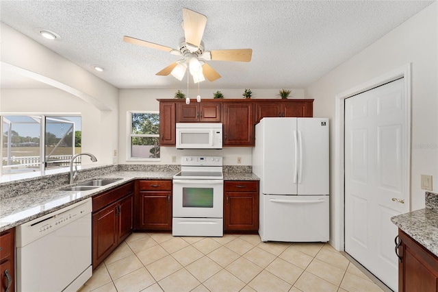 kitchen with light stone counters, white appliances, light tile patterned floors, a textured ceiling, and a sink