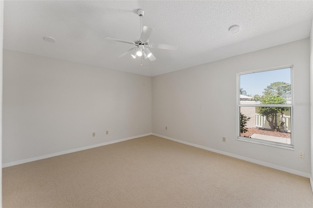 spare room with a textured ceiling, light colored carpet, baseboards, and a ceiling fan