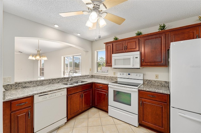 kitchen featuring white appliances, light tile patterned floors, a textured ceiling, arched walkways, and a sink