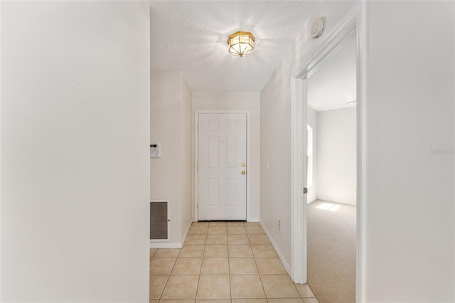 corridor featuring visible vents, baseboards, light tile patterned floors, and a textured ceiling