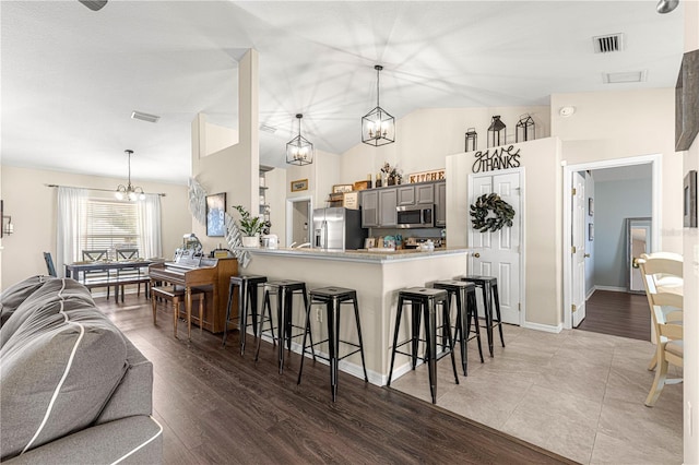 kitchen featuring gray cabinets, a kitchen breakfast bar, stainless steel appliances, a notable chandelier, and kitchen peninsula