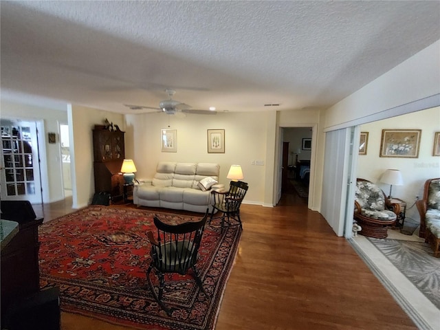 living room with ceiling fan, dark wood-type flooring, and a textured ceiling