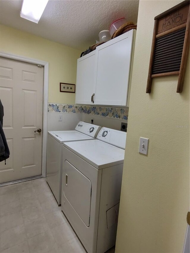 clothes washing area featuring a textured ceiling, cabinets, and washing machine and clothes dryer