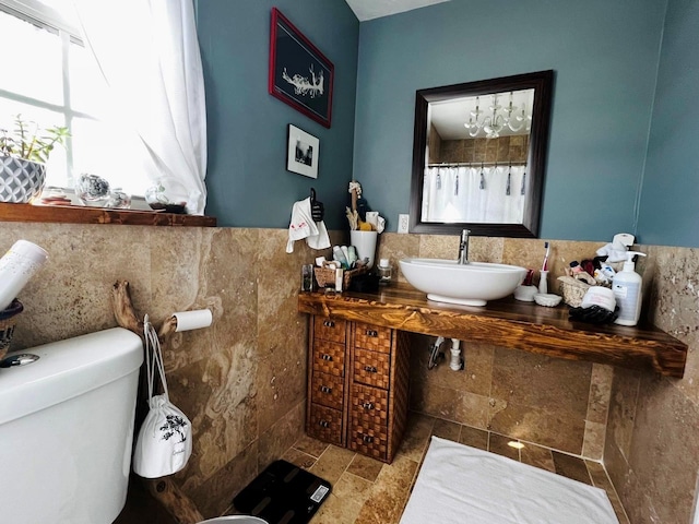 bathroom with a wainscoted wall, a sink, tile walls, and toilet