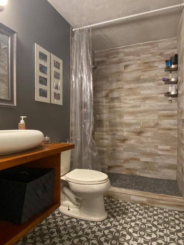 bathroom featuring toilet, a sink, tiled shower, and tile patterned floors