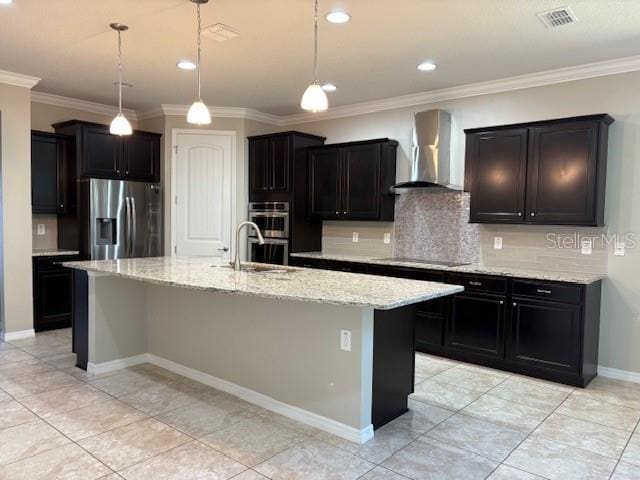 kitchen featuring sink, appliances with stainless steel finishes, an island with sink, pendant lighting, and wall chimney range hood