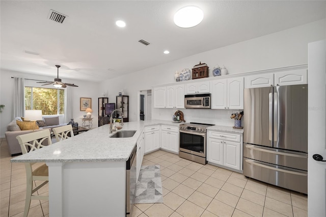 kitchen with appliances with stainless steel finishes, sink, a breakfast bar area, light stone counters, and kitchen peninsula