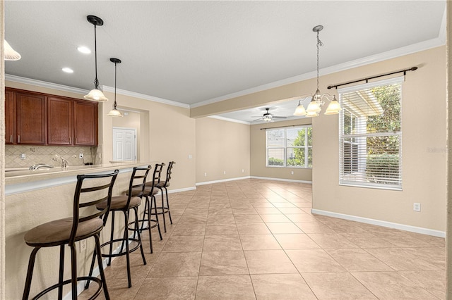 kitchen featuring pendant lighting, tasteful backsplash, a kitchen bar, ornamental molding, and light tile patterned floors