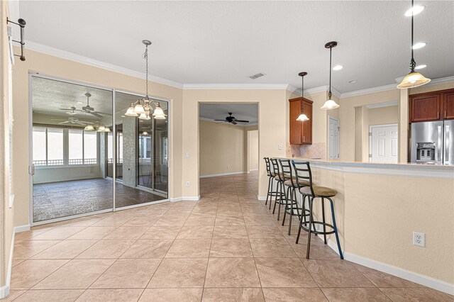 kitchen with tasteful backsplash, ornamental molding, stainless steel fridge, and hanging light fixtures