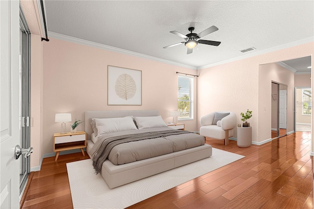 bedroom featuring hardwood / wood-style flooring, ornamental molding, multiple windows, and a textured ceiling