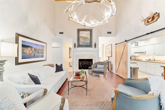 living room with wood-type flooring, a notable chandelier, a towering ceiling, a barn door, and a tiled fireplace