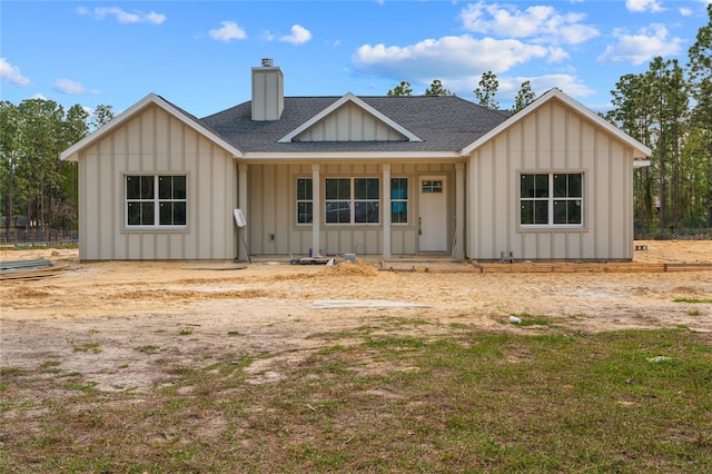 view of front of house featuring covered porch, a shingled roof, a chimney, and board and batten siding