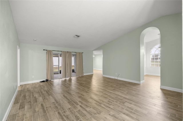 unfurnished living room with lofted ceiling, plenty of natural light, arched walkways, and light wood-style flooring