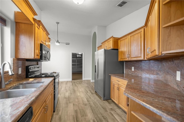 kitchen featuring brown cabinets, stainless steel appliances, visible vents, a sink, and dark stone counters