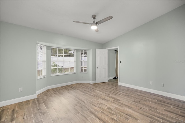 empty room featuring lofted ceiling, light wood-style flooring, baseboards, and a ceiling fan