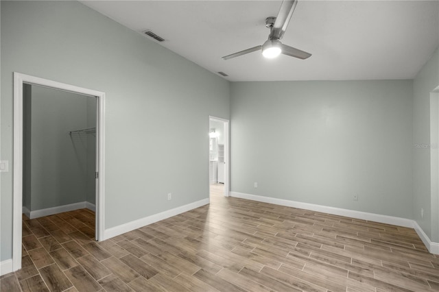 unfurnished bedroom with light wood finished floors, visible vents, a spacious closet, vaulted ceiling, and baseboards